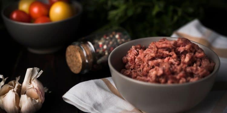 Carne moída em uma tigela com alho e vegetais atrás.