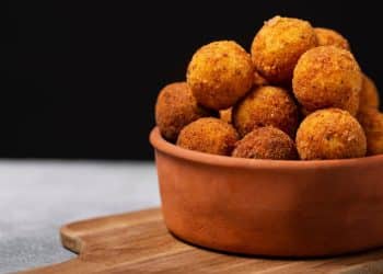 Bolinho de arroz em tigela marrom em frente a um fundo preto.