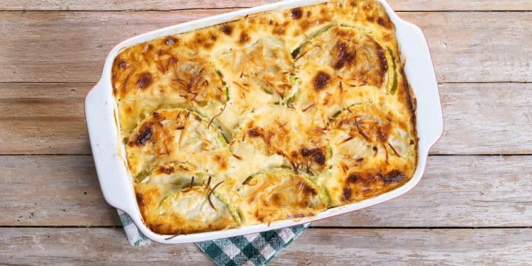 Assadeira de gratinado de frango em cima de um pano em uma mesa de madeira.