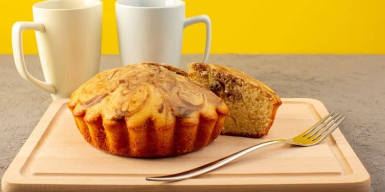 Bolo de caneca fit em uma tábua de madeira ao lado de duas xícaras em um fundo amarelo.