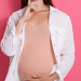 Mulher grávida com a mão na barriga, a imagem está em um fundo rosa.