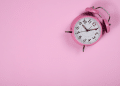 Relógio que remete um alarme em uma parede de fundo rosa