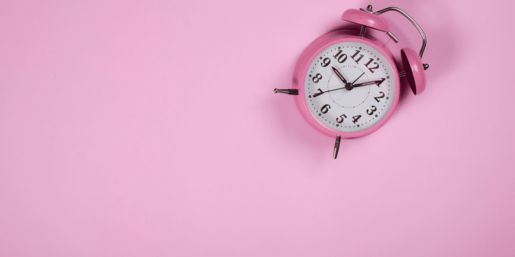 Relógio que remete um alarme em uma parede de fundo rosa