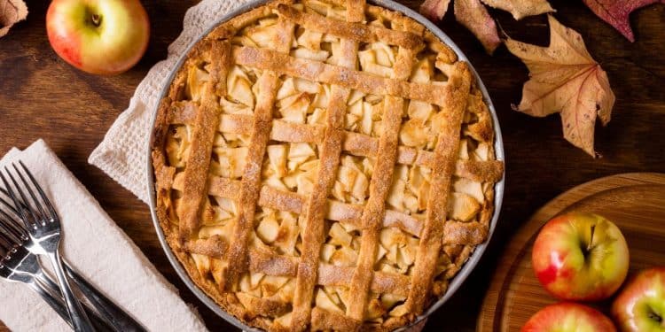 Torta de maçã com talheres, maçãs e folhas em volta.