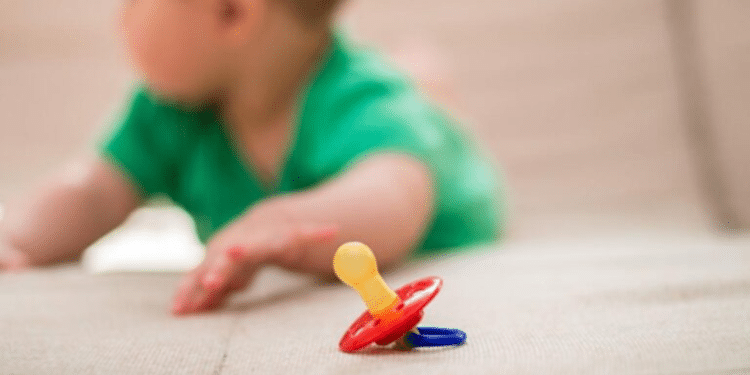 Criança próximo a chupeta que está no chão