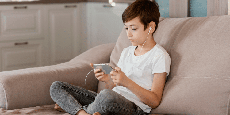 Criança sentada no sofá, usando fones de ouvido e mexendo no celular
