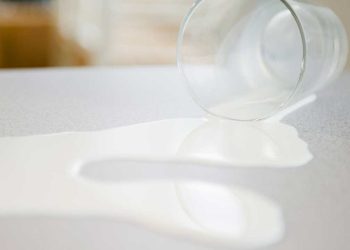 Copo de vidro com leite escorrendo de dentro, virado na mesa