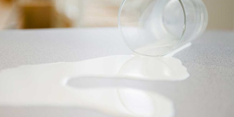 Copo de vidro com leite escorrendo de dentro, virado na mesa