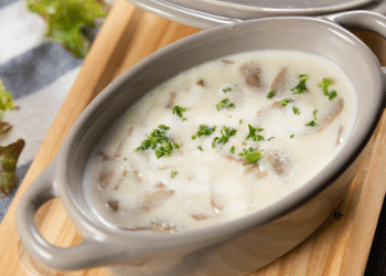 Molho branco numa travessa, com temperos em cima e uma tabua embaixo.